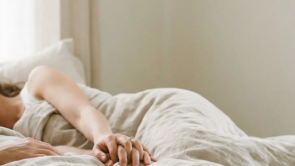 Couple adulte allongé sous des draps clairs, lumière douce du matin, ambiance intime et apaisée avec de l’espace vide sur un côté.